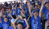  Kids jumping out of their seats and screaming with excitement at an outdoor baseball game.